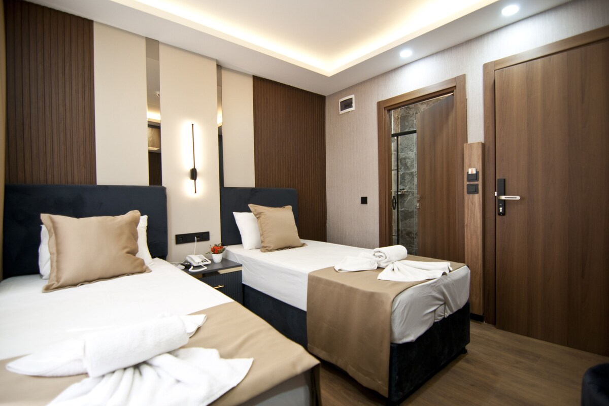 A hotel room with two beds, wooden paneling, a stone accent wall, and a wooden door.