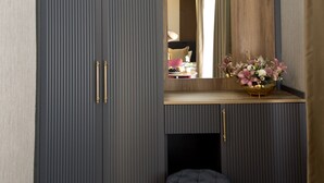 Una stanza moderna con un armadio grigio, una piccola panca e uno specchio che riflette un letto e un comodino.