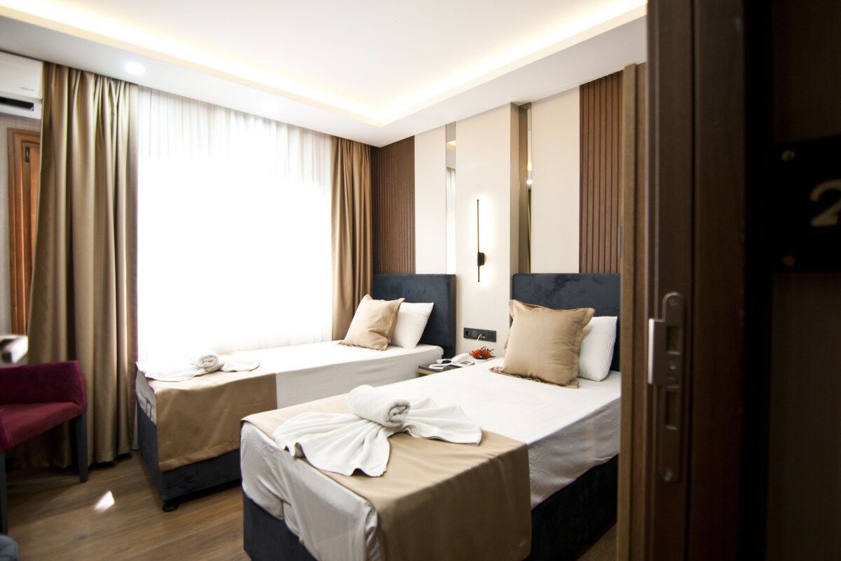 A hotel room with two beds, a red chair, and a door with a number.
