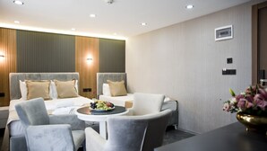 Una moderna camera d'albergo con un letto grande, due poltrone, un tavolino con della frutta e un vaso con fiori.