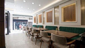 Un ristorante moderno con tavoli in legno e panche imbottite verdi, illuminazione a soffitto incassata e vista sulla strada.