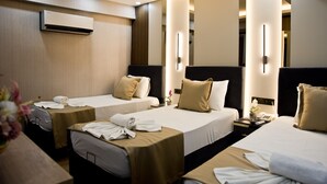 Una camera d'albergo con due letti, un comodino con un telefono e un vaso di fiori, e un condizionatore d'aria a parete.