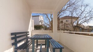 Een balkon met een houten tafel en bankjes, met uitzicht op een woonwijk met gebouwen en bomen.