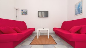 Een kamer met twee rode banken, een witte tafel en een klein vloerkleed.