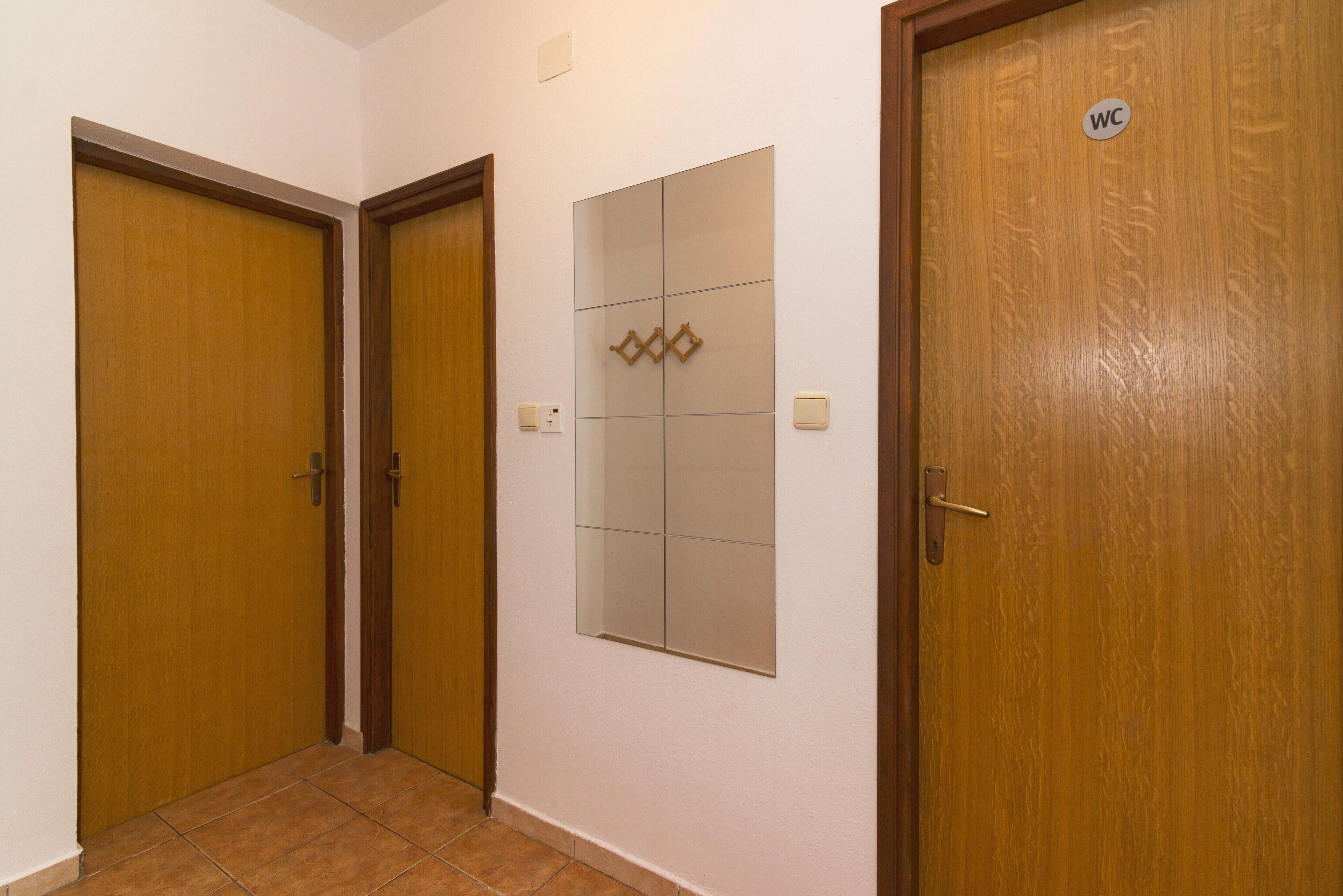 Un corridoio con tre porte in legno, una delle quali contrassegnata con il simbolo ‘WC’, e uno specchio fissato alla parete.