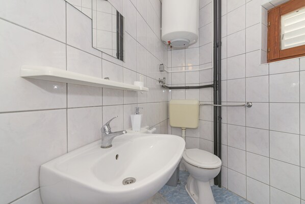 A bathroom with a white sink, toilet, and a white toilet paper holder on a white tiled wall.