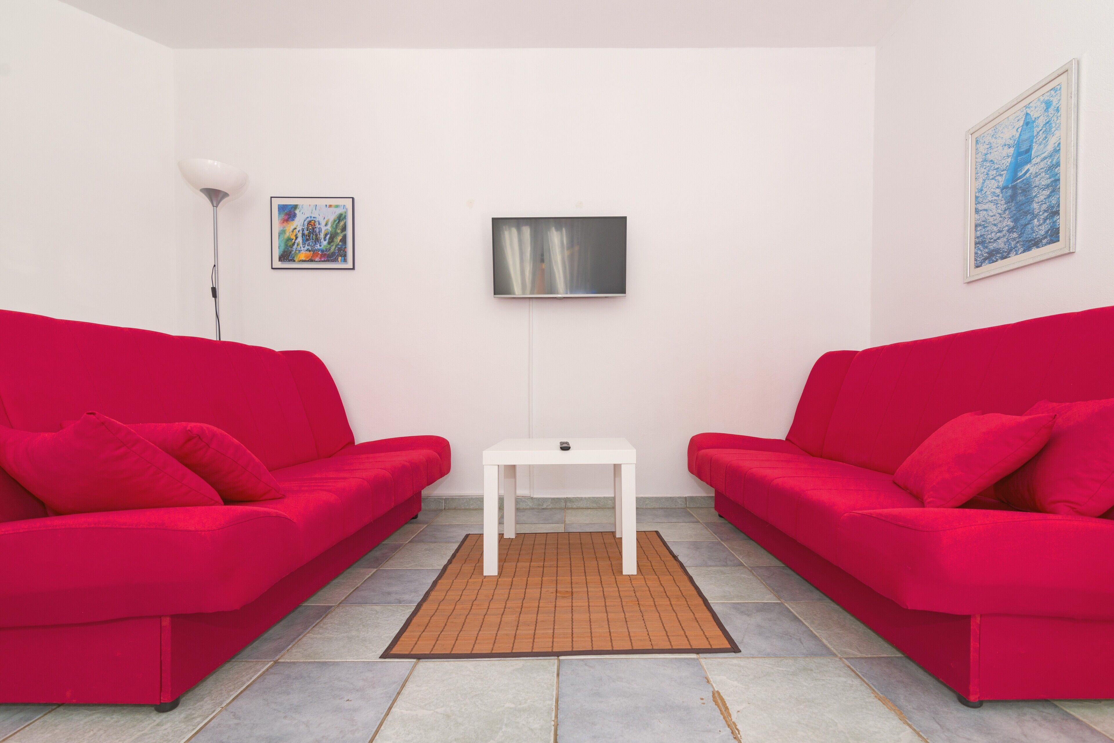 Um quarto com dois sofás vermelhos, uma mesa branca e um tapete pequeno.