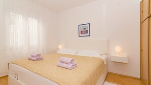 En snyggt bäddad säng med en beige pläd och två hopvikta handdukar, ett sängbord med en lampa och en inramad tavla på väggen.