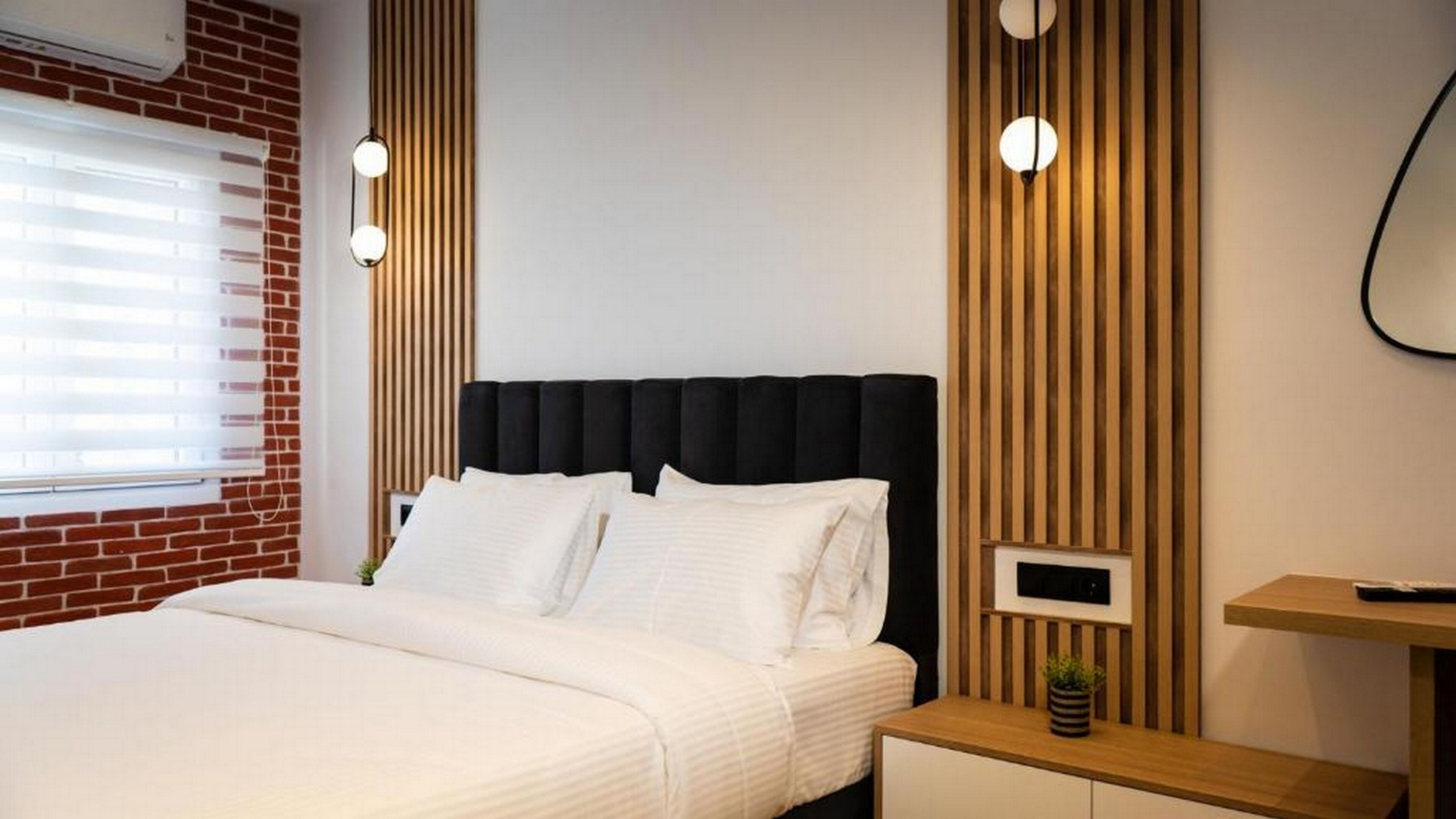 A modern bedroom with a black upholstered headboard, white bedding, and wooden paneling on the walls.