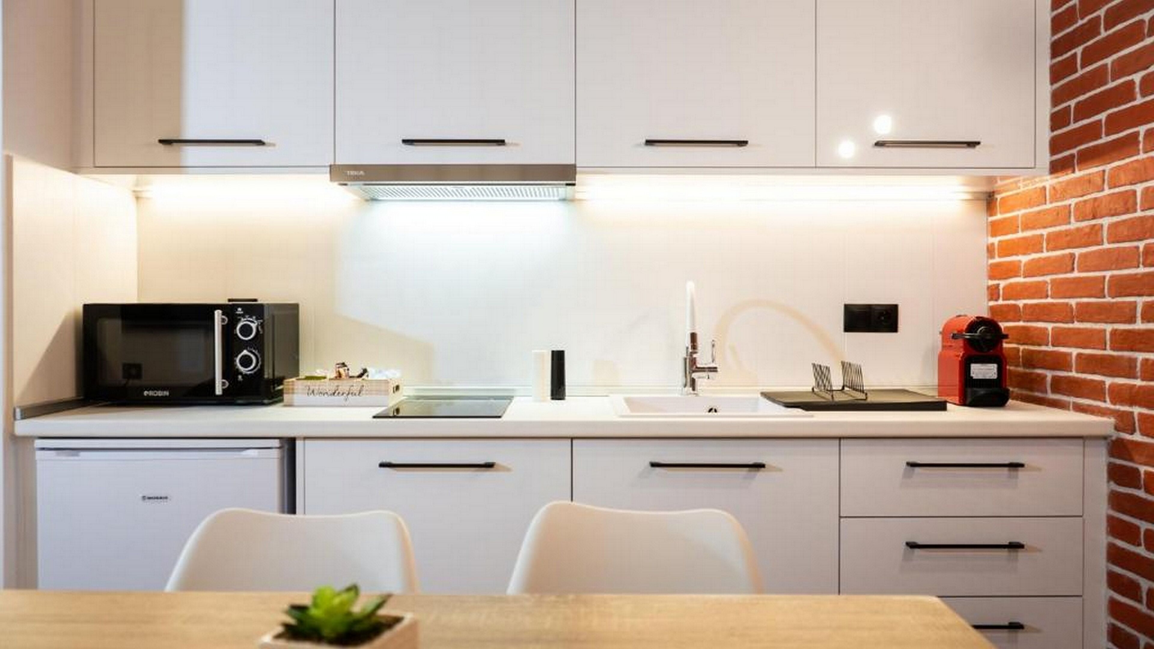 A modern kitchen with white cabinets, a microwave, a sink, and a red coffee machine.