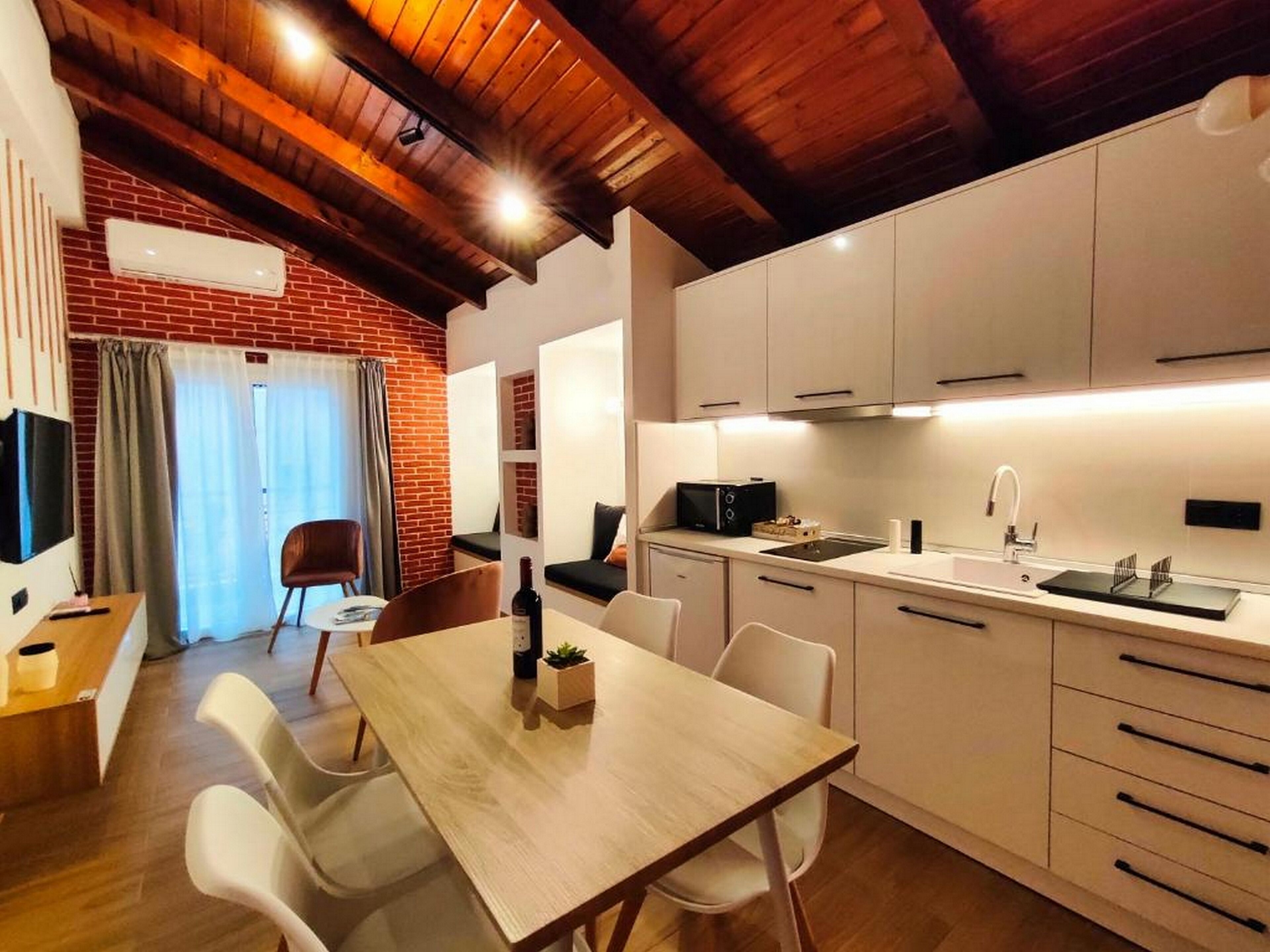 A modern kitchen with white cabinets, a wooden dining table, and a brick wall.