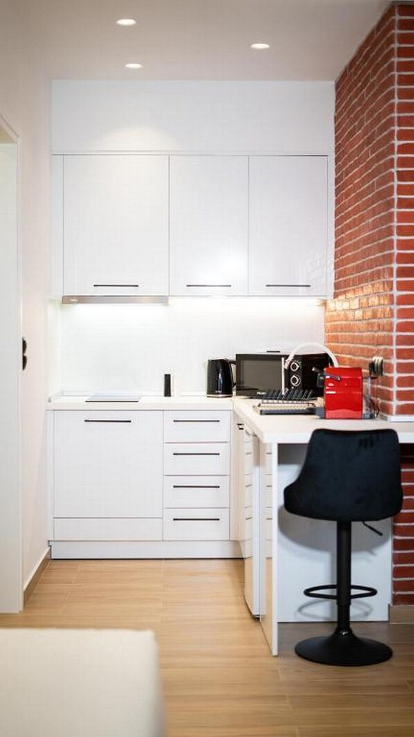A compact kitchen with white cabinetry, a coffee machine, and a black chair.