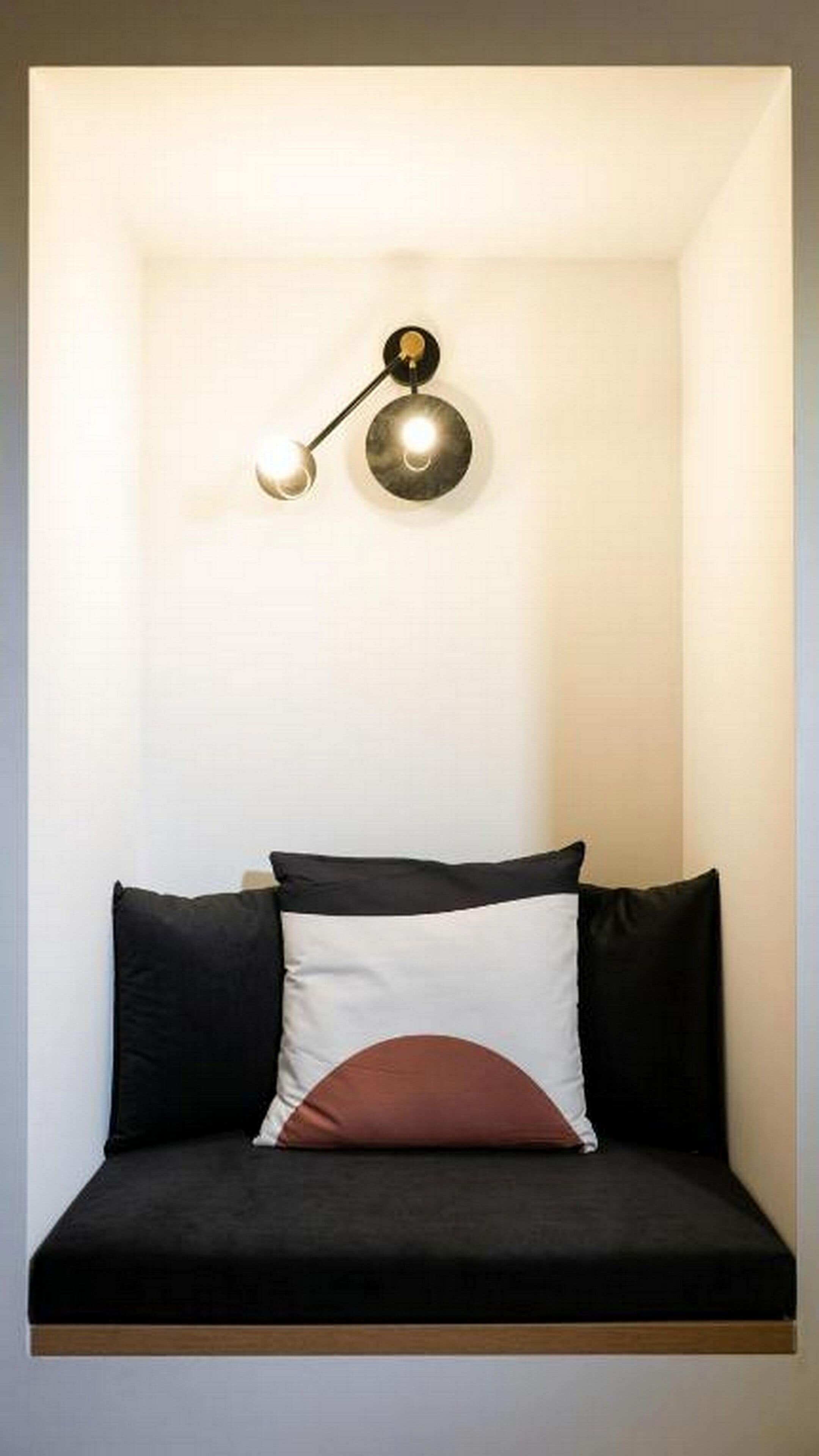 A minimalist room with a black and white sofa, a single round wall lamp, and a plain white wall.