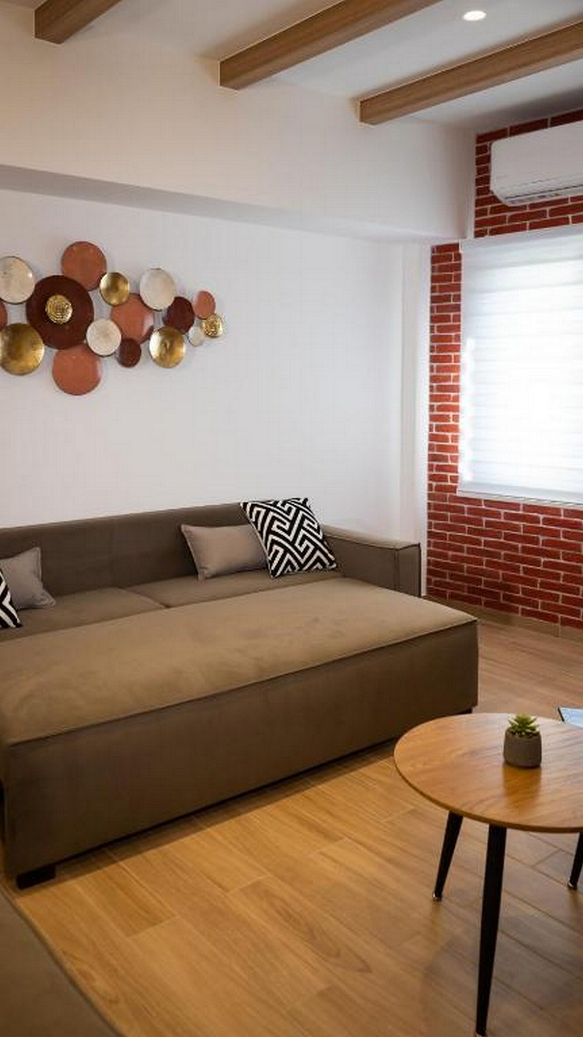 A modern living room with a brown sofa, a round wooden coffee table, and a decorative wall piece.