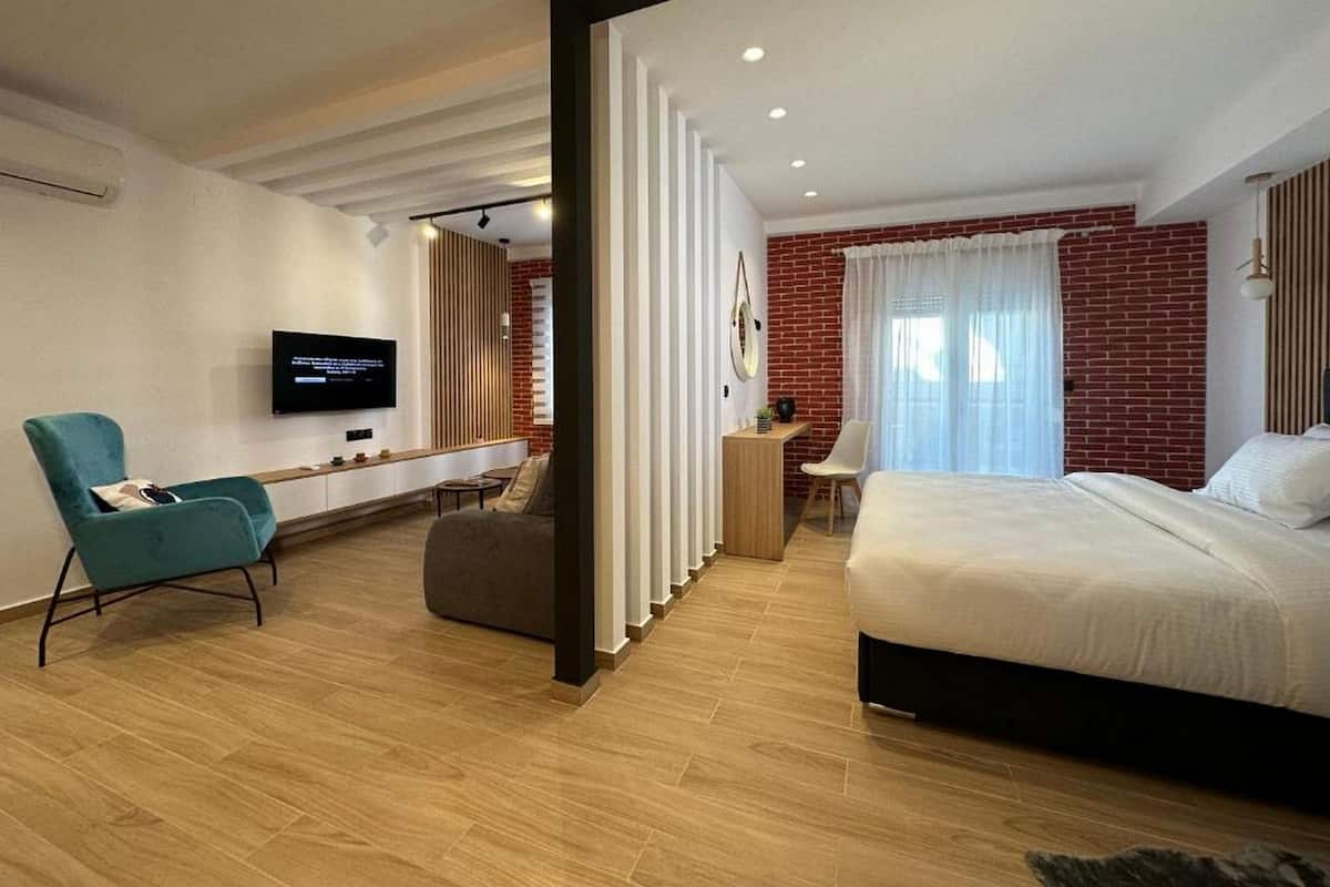A modern hotel room with a large bed, a TV, a desk, and a seating area.