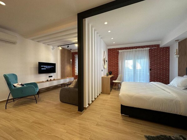 A modern hotel room with a large bed, a TV, a desk, and a seating area. - Centro Urban Suites (Kalabaka)