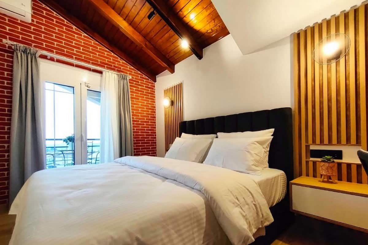 A hotel room with a large bed, a wooden ceiling, a brick wall, and a view of the outdoors.