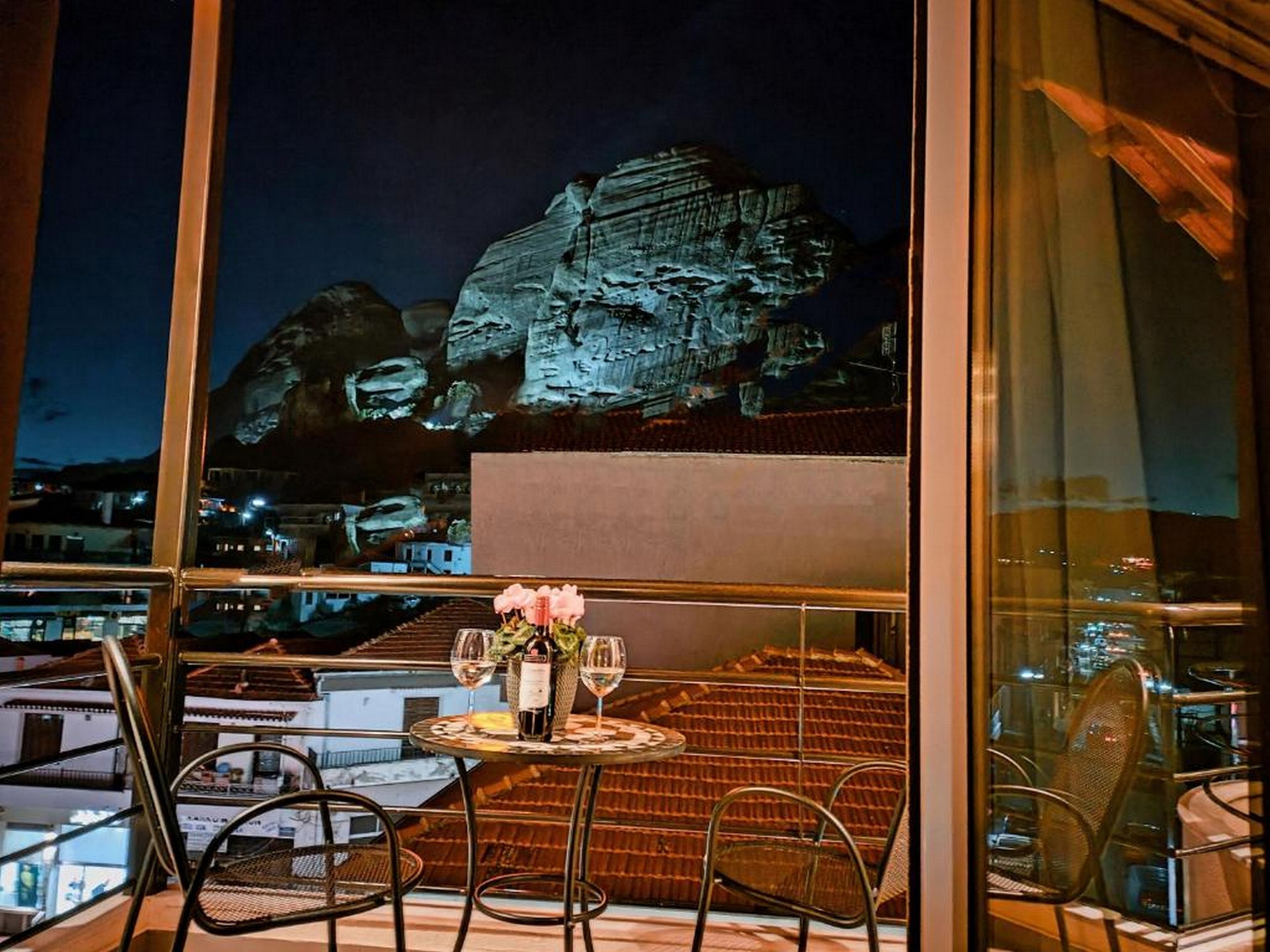 A balcony with a table set for two, a bottle of wine, and a vase of flowers.