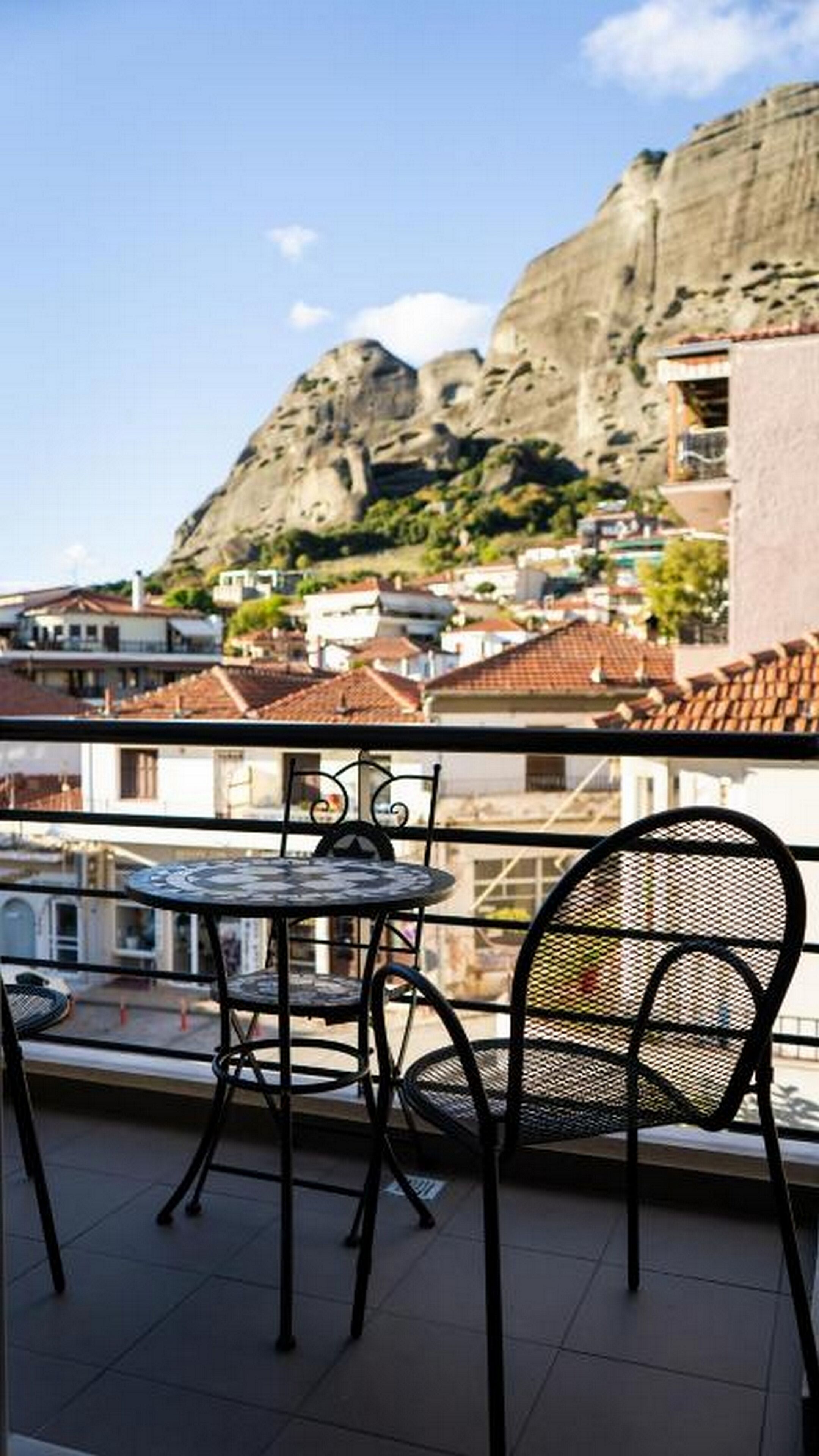 A balcony with a table and chairs overlooking a town with buildings and a mountain in the background.