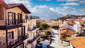 A multi-story building with balconies, a street view, and a mountain in the background. - Centro Urban Suites (Kalabaka)