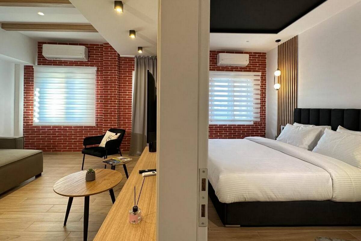 A modern hotel room with a brick wall, a bed, a sofa, a small round table, and a television.