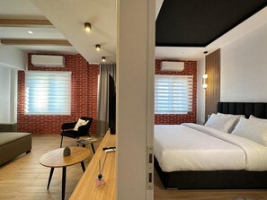 A modern hotel room with a brick wall, a bed, a sofa, a small round table, and a television. - Centro Urban Suites (Kalabaka)