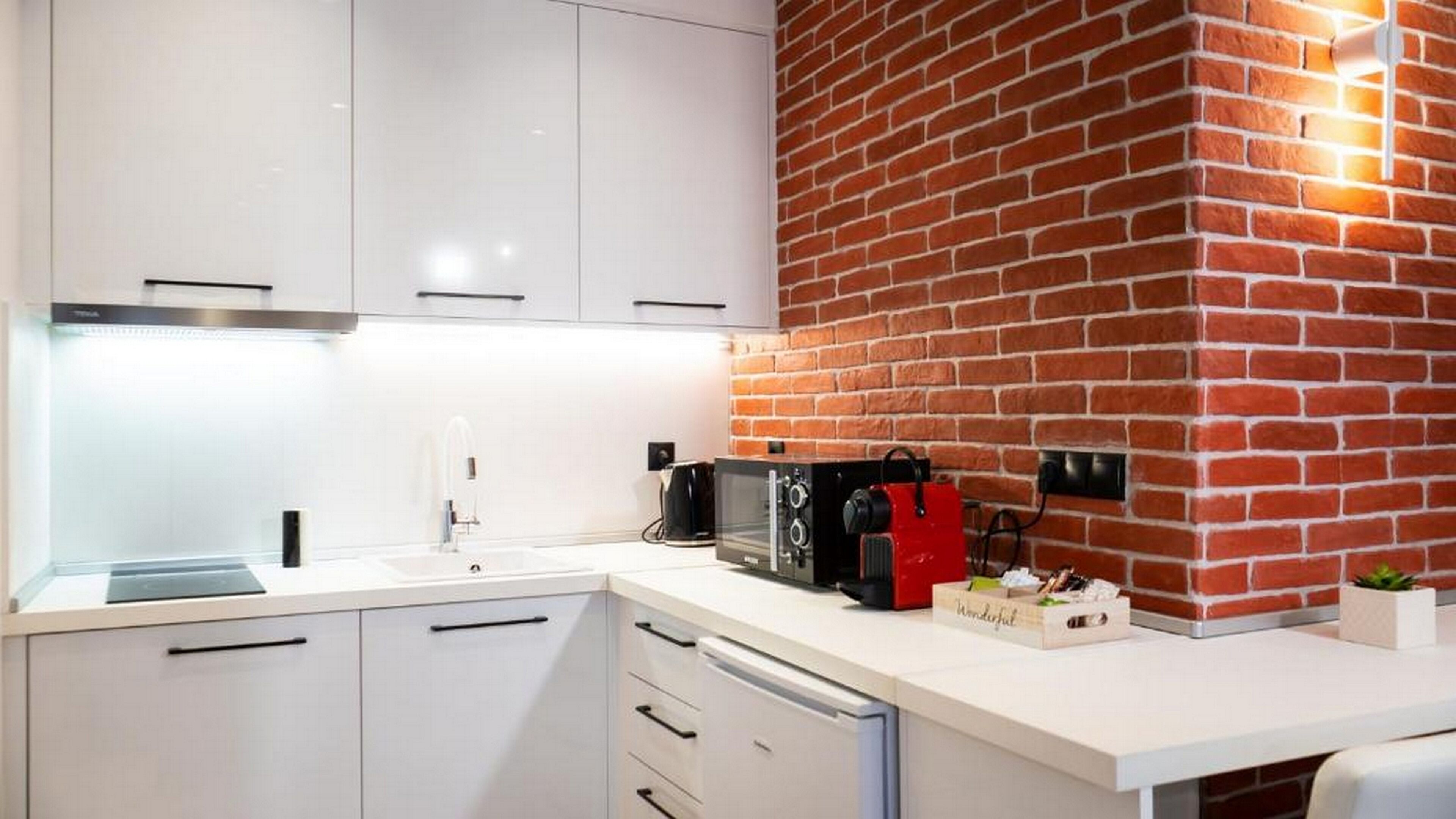 Una cocina moderna con armarios blancos, una pared de acento de ladrillo, microondas integrado y una cafetera.