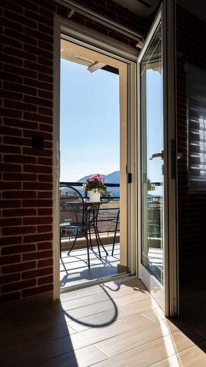 A sliding glass door leading to a balcony with a table and chairs, a potted plant, and a view of the sky and mountains. - Centro Urban Suites (Kalabaka)