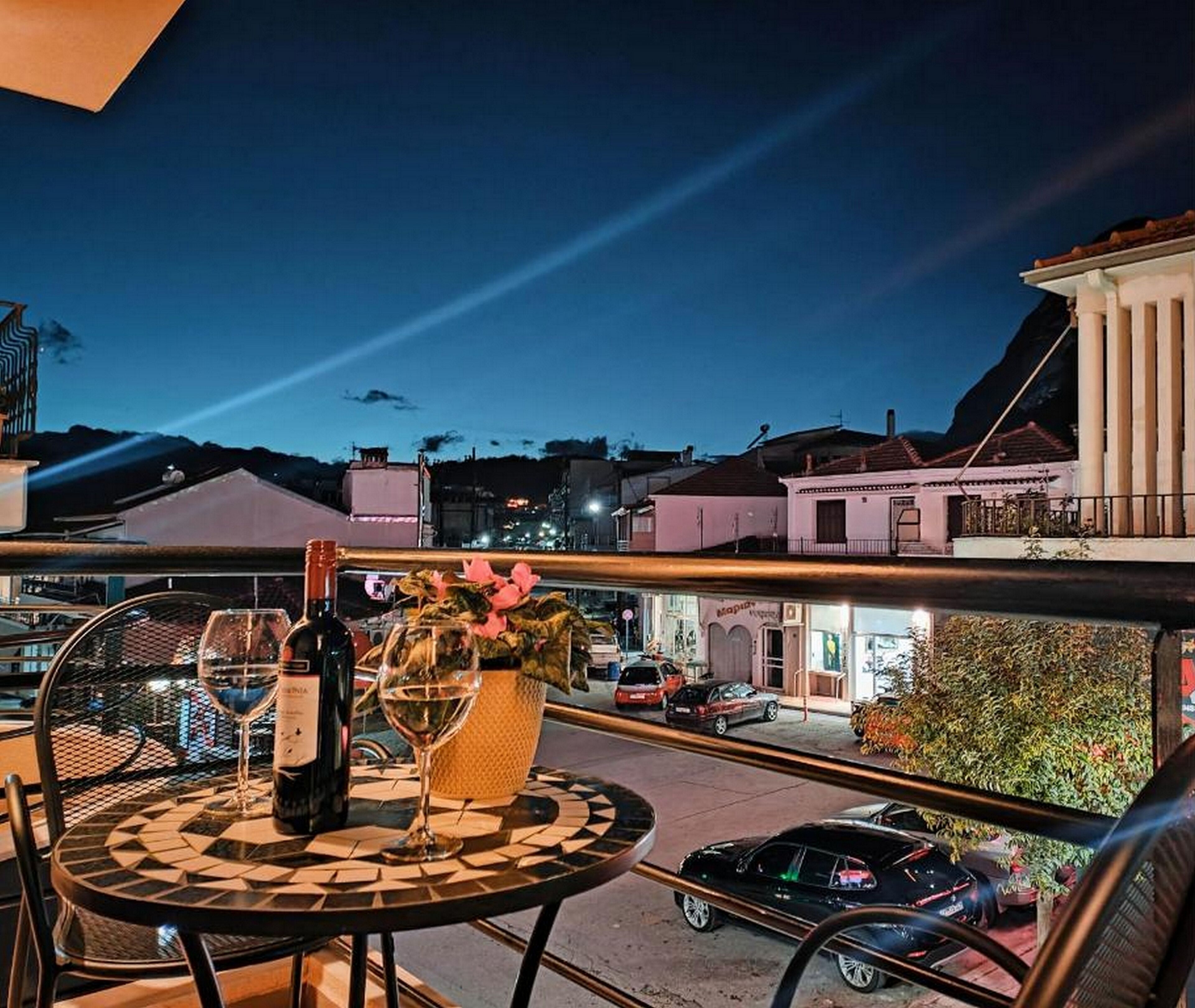 A balcony with a table, chairs, a bottle of wine, and a vase of flowers.