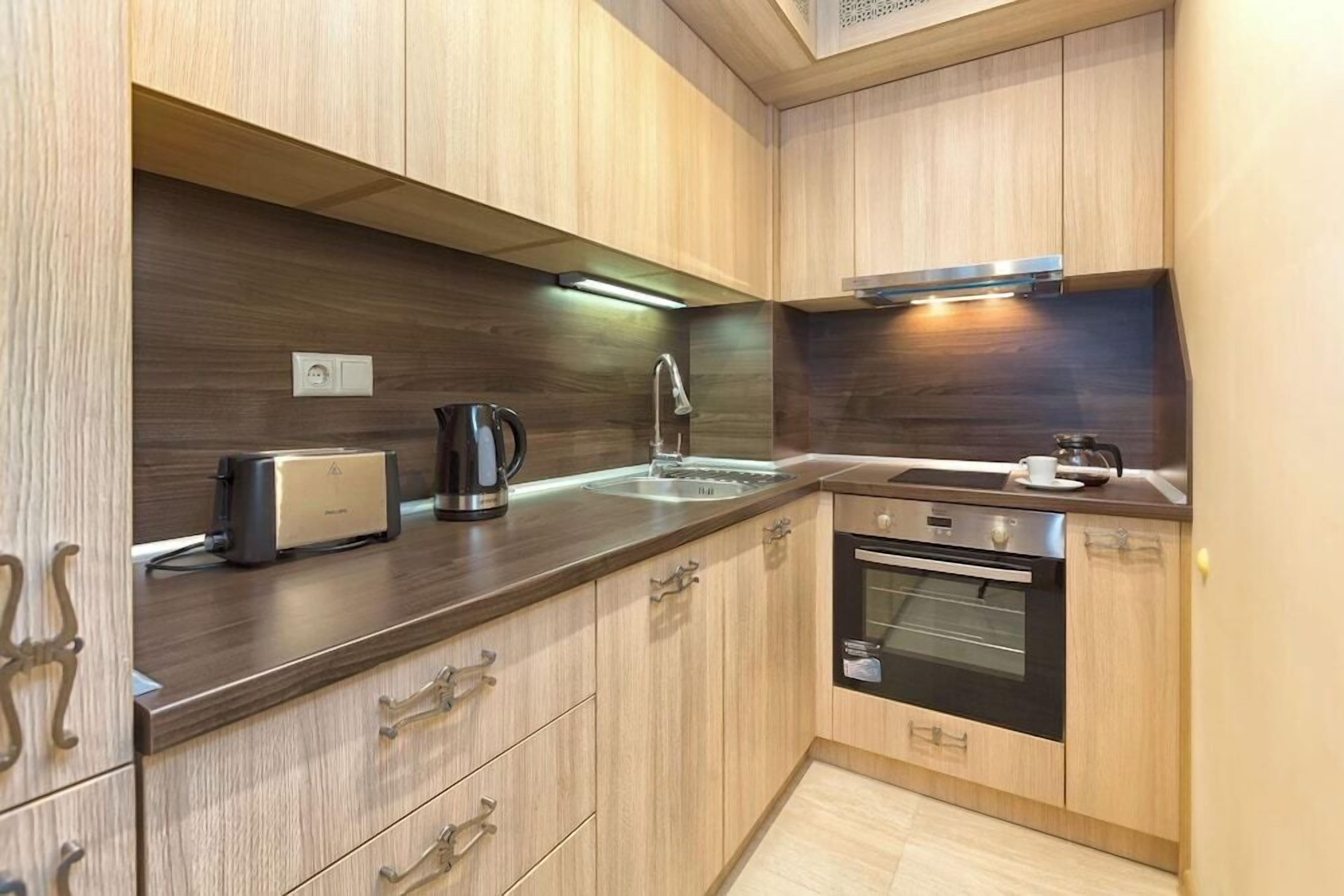 A modern kitchen with wooden cabinets, a built-in oven, a coffee maker, and a kettle.