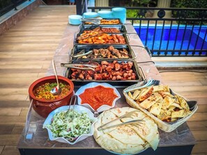 Une table de buffet garnie de divers plats, avec une piscine en arrière-plan.