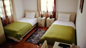 A double room with two beds, bedside tables with lamps, a rug, and a window with curtains. - Hotel Belgrad Mangalem (Berat)