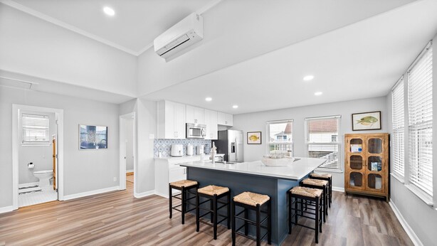 Une cuisine moderne avec des meubles blancs, un îlot central doté de tabourets de bar et un meuble en bois avec des portes en verre.