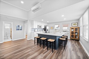 Une cuisine moderne avec des meubles blancs, un îlot central doté de tabourets de bar et un meuble en bois avec des portes en verre.
