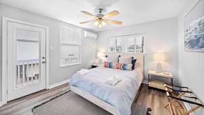 Une chambre à coucher comprenant un lit, un ventilateur de plafond, une table de chevet, une lampe et une fenêtre avec des stores.