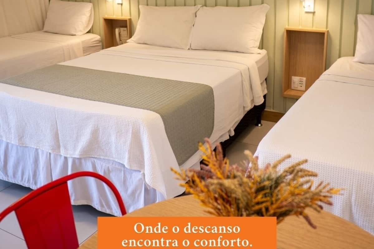 Ein Hotelzimmer mit zwei Betten, einem Holznachttisch, einem roten Stuhl und einer Vase mit Trockenblumen.
