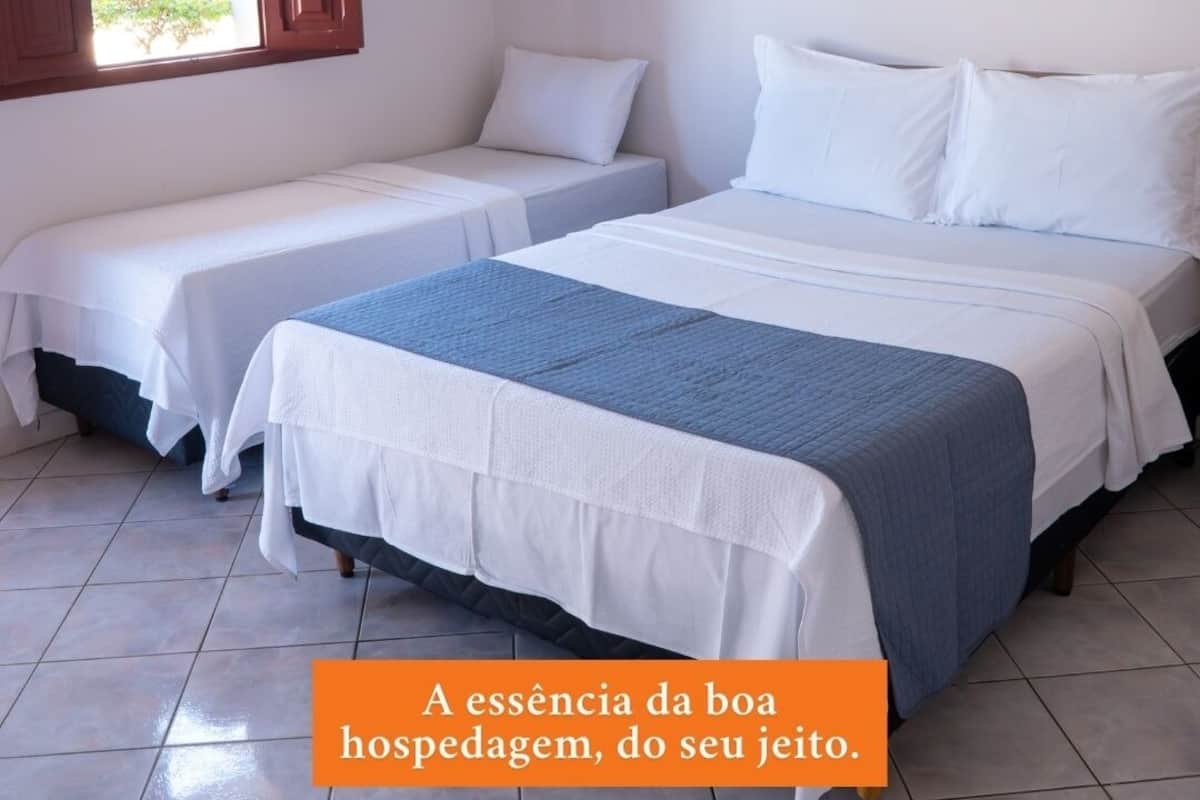 Ein Hotelzimmer mit zwei Betten, einem Fenster mit Holzjalousien und einem Fliesenboden.