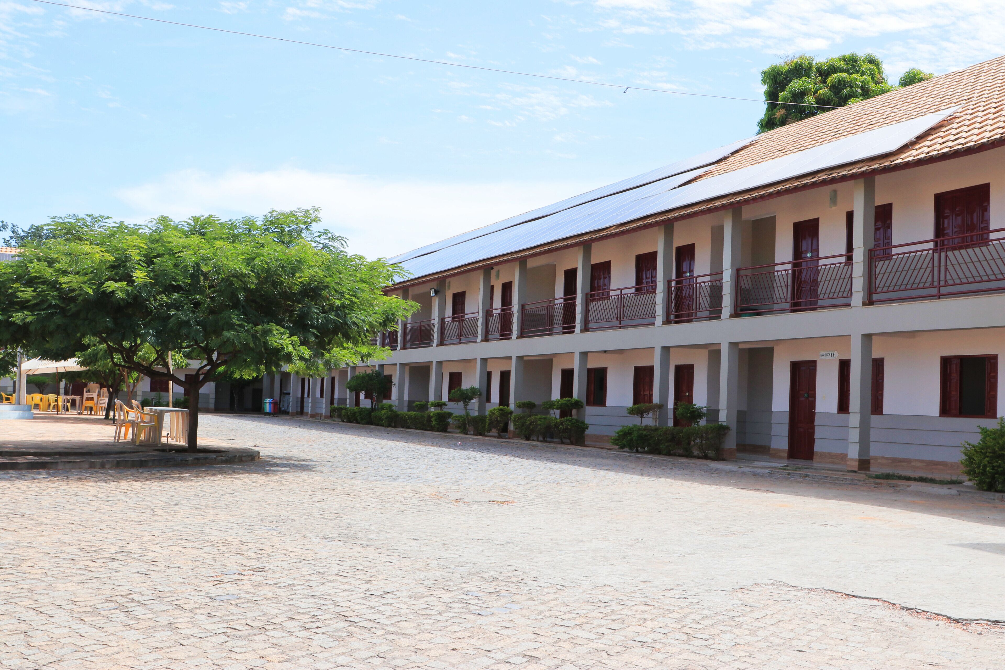 A two-story building with a tiled roof, multiple balconies, and a paved courtyard.