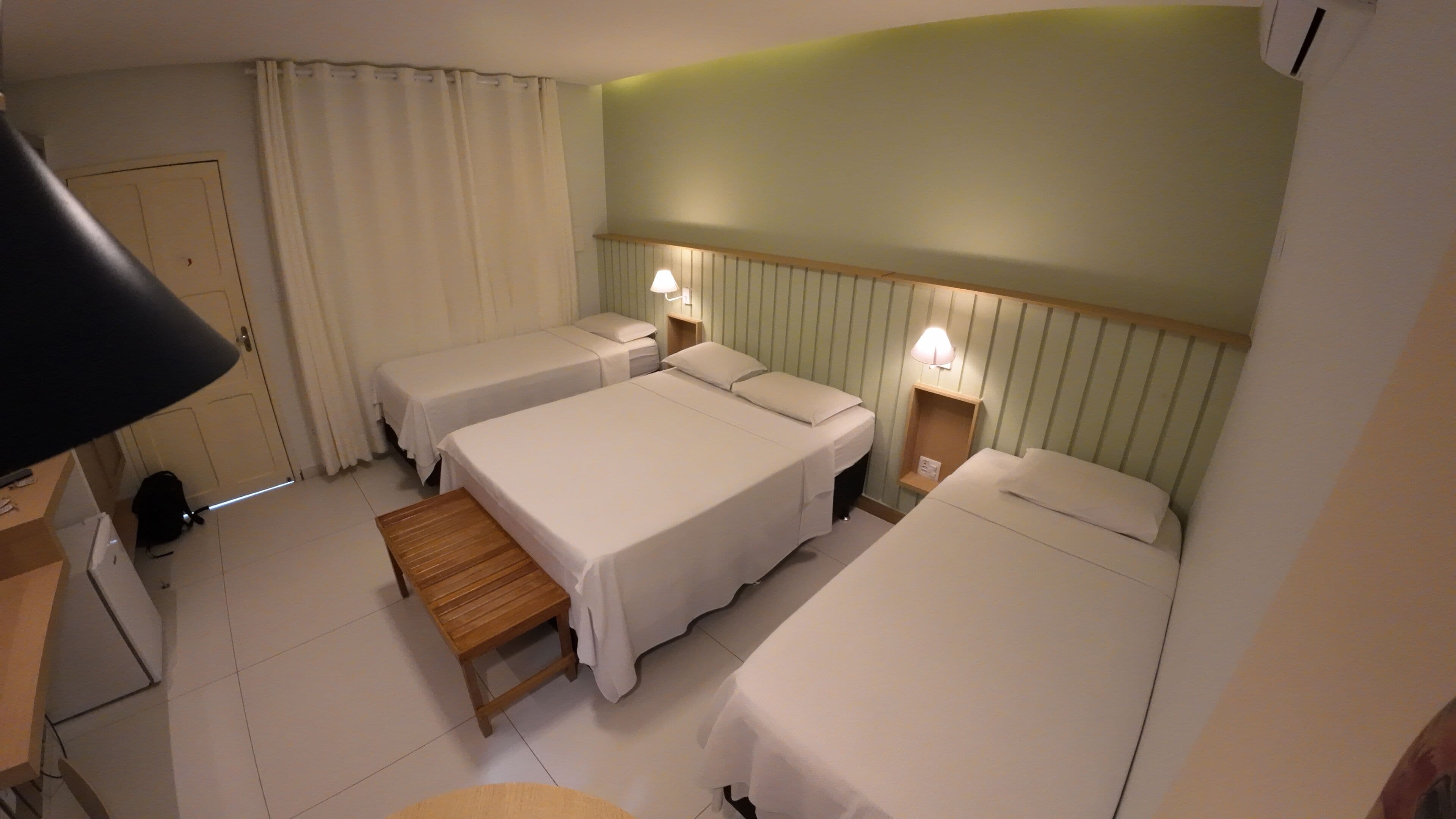 Una habitación de hotel con dos camas individuales, un banco de madera, un escritorio con lámpara y un armario.