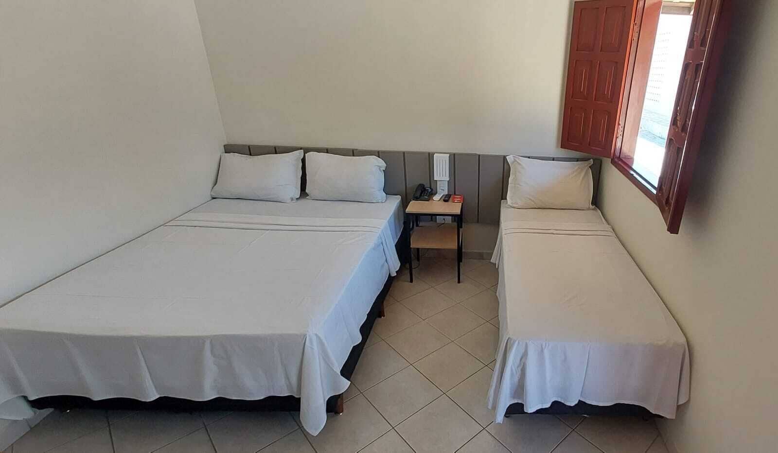 A room with two single beds, a small table with a chair, and a window with a wooden shutter.