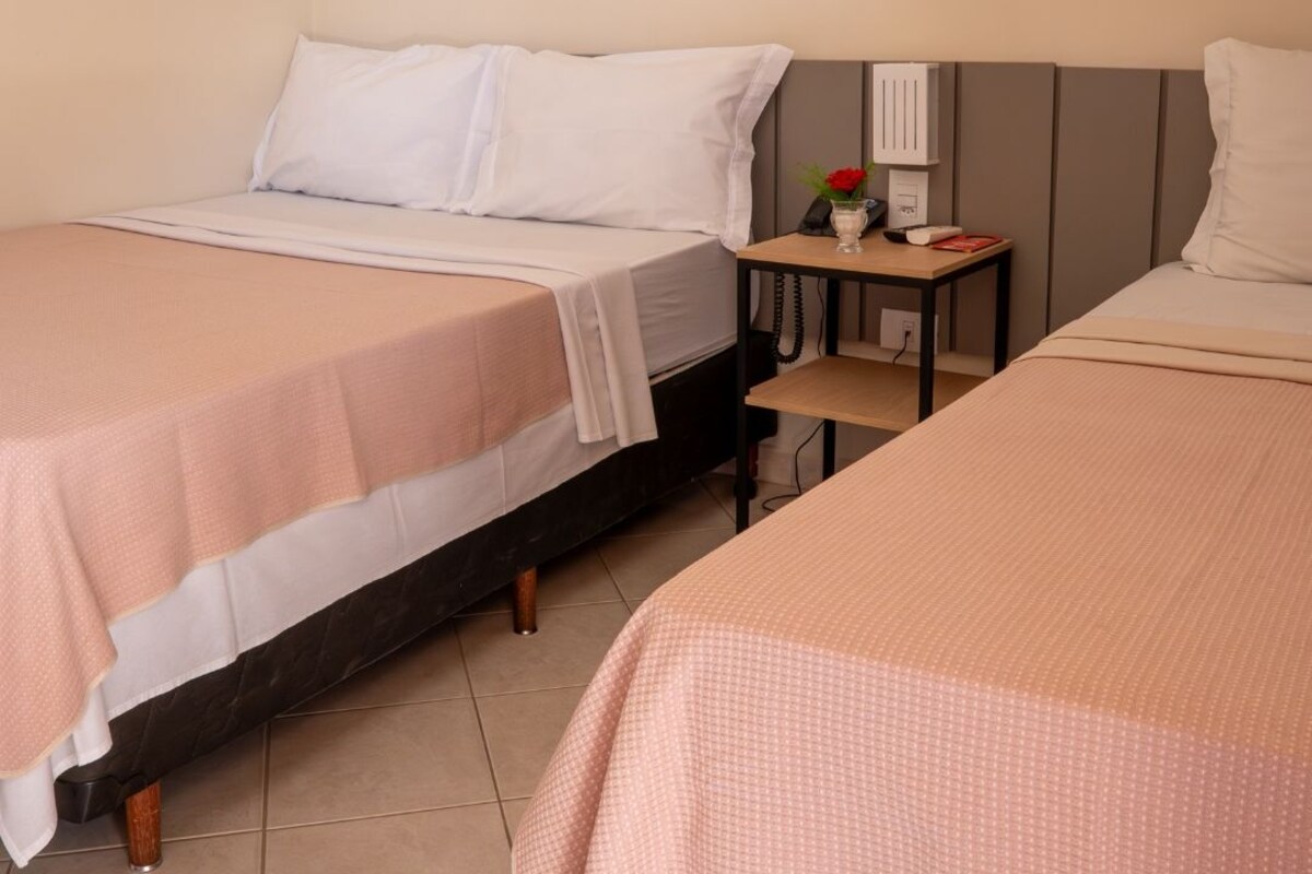 A hotel room with two beds, a nightstand with a lamp, and a small table with a vase of flowers.