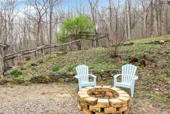 Sit by the fire pit surrounded by Adirondack chairs in a serene natural setting.