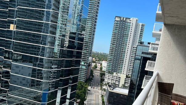 Um edifício alto com fachada de vidro moderna, uma varanda com mobiliário de vime e vista clara da rua.