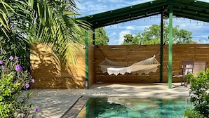 Un'area esterna riparata con piscina, recinzione in legno e un'amaca.