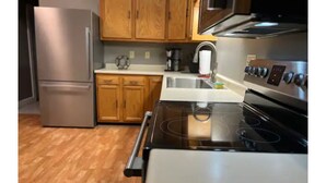 A kitchen with wooden cabinets, a stainless steel refrigerator, a stove, and a microwave. - IU Medical Campus Convenience (Indianapolis)