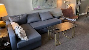 A modern living room with a grey sectional sofa, a small round table, and a brown leather chair. - IU Medical Campus Convenience (Indianapolis)