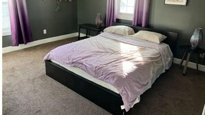 A bedroom with a bed, two nightstands, a window with curtains, a wall art piece, and a vase on one of the nightstands. - IU Medical Campus Convenience (Indianapolis)