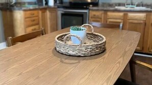 A wooden dining table with a woven basket containing a white mug. - IU Medical Cozy Campus Castle (Indianapolis)