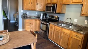 A kitchen with wooden cabinets, a stainless steel sink, a microwave, and an oven. - IU Medical Cozy Campus Castle (Indianapolis)