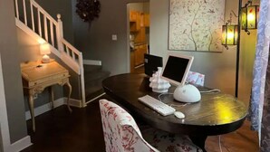A home office with a desk, computer, keyboard, and mouse. There is a staircase and a wall with a tree painting. - IU Medical Cozy Campus Castle (Indianapolis)